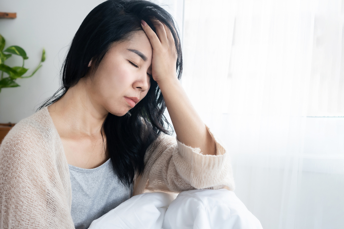 Asian woman having headache migraine, hangover, lack of sleep sitting in bed